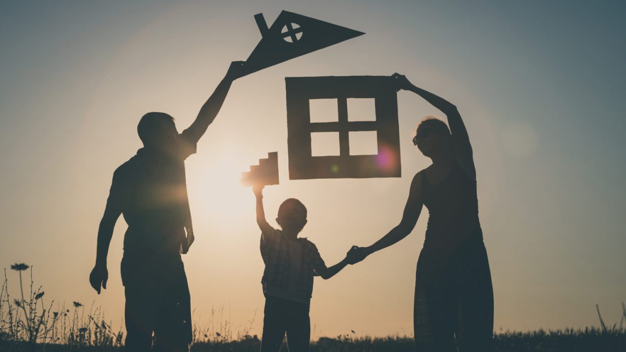 Happy family standing on the field at the sunset time. They build a house. Concept of friendly family.